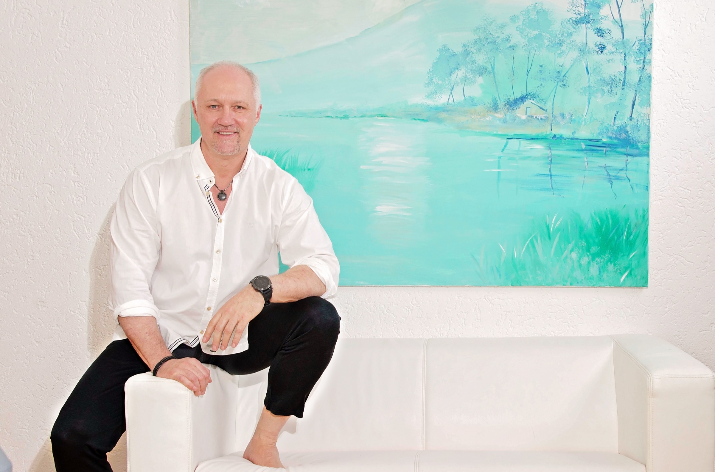 Andr&eacute; Dennes entspannt auf dem Sofa, barfuss &mdash; vor einem Gem&auml;lde in Wasserfarben