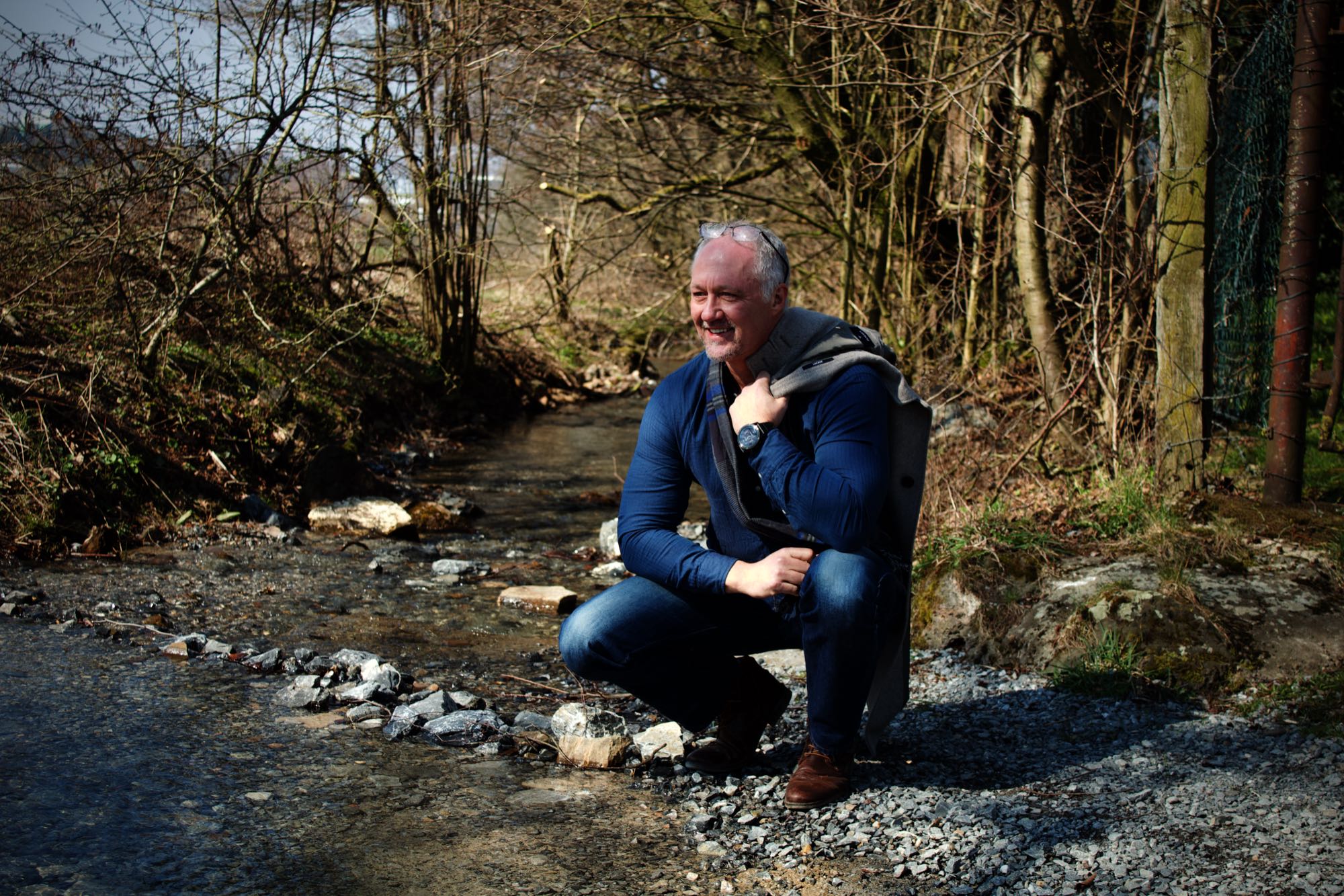 Andr&eacute; Dennes hockt an einem Bachlauf in der Natur &mdash; Fr&uuml;hjahrslicht, ruhiger Moment